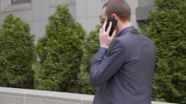 Genç bir işadamı sokakta yürürken mutlu bir telefon görüşmesi iletişim kurar. Elinde bir bardak kahve ile takım elbiseli neşeli bir adam akıllı telefonda konuşurken gülümsüyor. 4k görüntü.