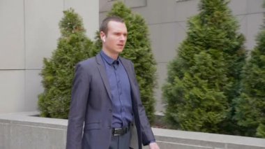 Genç işadamı, kablosuz kulaklıkla sokakta yürüyor ve telefonda agresif bir şekilde tartışmayı yönetiyor. Klasik takım elbiseli adam telefonda konuşarak öfkesini gösteriyor. 4k görüntü