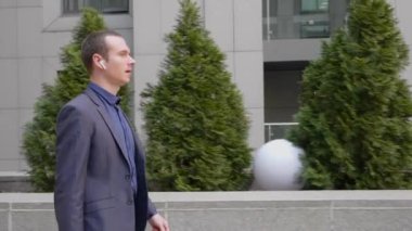 Kablosuz kulaklıkla yürüyen ve telefon görüşmesi üzerinden konuşan genç bir işadamı. Elinde akıllı telefon olan klasik takım elbiseli bir adam bir sohbete öncülük ediyor. 4k görüntü.
