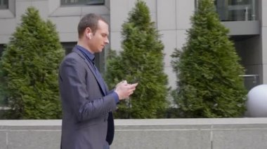 Genç işadamı kulaklarında kablosuz kulaklıklar ile gider ve Smartphone bir mesaj çevirir. Takım elbiseli adam kablosuz kulaklıklar aracılığıyla müzik dinler ve telefonda metin yazıyor. 4k görüntüleri