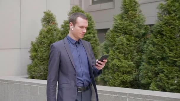 Joven Hombre Negocios Caminando Por Calle Con Auriculares Inalámbricos Escribir — Vídeo de stock