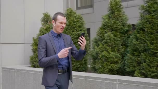 Joven Hombre Negocios Camina Con Auriculares Inalámbricos Dirige Agresivamente Una — Vídeo de stock