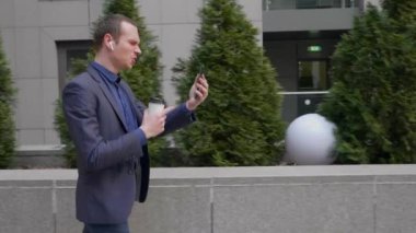 Genç işadamı kablosuz kulaklıkla yürüyor ve akıllı telefondaki bir video görüşmesini agresif bir şekilde yönetiyor. Elinde bir bardak kahve olan bir adam video konferansında hoşnutsuzluğunu gösterir..