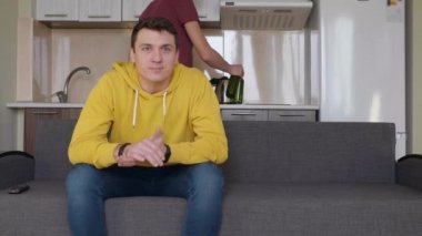 Bira şişeleriyle futbol maçı izleyen iki adam. Adam bir içki getiriyor, arkadaşının yanında oturuyor ve dikkatlice televizyon izliyor. Arka planda bir mutfak. 4k görüntü.
