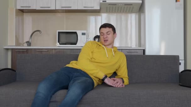 一个男人正在沙发上休息 一个年轻人坐在一个坐的的躺在一个地说话 背景上的厨房 — 图库视频影像