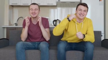 İki adam Tv'de bir futbol maçı izliyor. Arkadaşlar dinlensin. Arka planda bir mutfak. 4k görüntü.