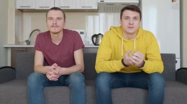 İki adam tv'de bir futbol maçı izlemek ve en sevdikleri takımın zaferinin tadını çıkarın. Genç çocuklar kanepede oturuyor, oyunun önemli anı hakkında endişe ve zafer sevinmek. 4k görüntü.