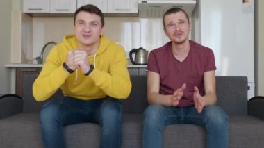 Kanepede oturan iki adam televizyonda bir futbol maçı izlemek ve farklı takımlara destek. Kaybeden takım için destek olan adam kazanan takımın bir hayranı olan arkadaşını iter. 4k görüntü.