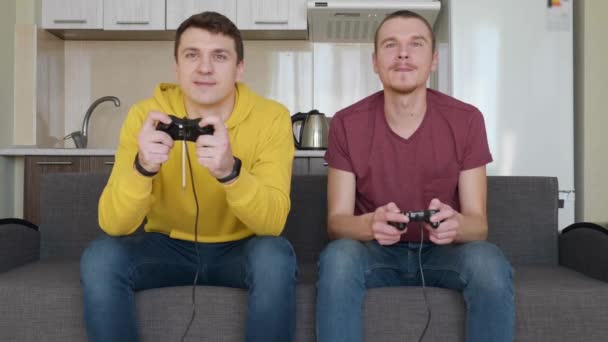 两个人正在玩电子游戏并获胜 年轻人坐在沙发上 手里拿着游戏板 玩游戏机 享受胜利 给对方五个 团队匹配 — 图库视频影像