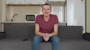 Bir adam televizyon izliyor. Kanepede oturan neşeli bir genç adam ve sert gülüyor. Arka planda bir mutfak. 4k görüntü.