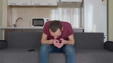 Bir adam televizyon izliyor. Kanepede oturan neşeli bir genç adam, sert gülüyor ve televizyon programı tartışıyor. Arka planda bir mutfak. 4k görüntü.