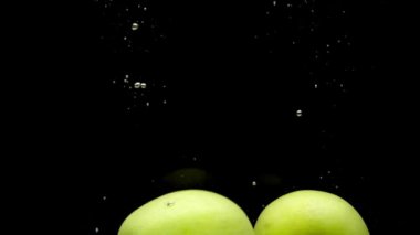 İki sarı elma siyah arka plan üzerinde şeffaf suya düşüyor. Akvaryumda sıçrayan taze meyveler ve meyveler. Organik meyveler, sağlıklı yiyecekler, diyet, hava kabarcıkları. Yavaş Çekim. Close