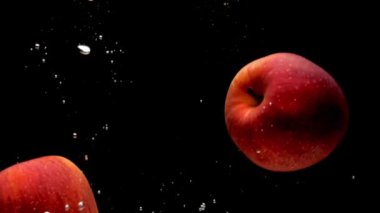 Siyah arka plan üzerinde şeffaf suya düşen iki kırmızı elma. Akvaryumda sıçrayan taze meyveler ve meyveler. Organik meyveler, sağlıklı yiyecekler, diyet, hava kabarcıkları. Yavaş Çekim. Close