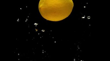 Sarı limon siyah arkaplanda şeffaf suya düşüyor. Akvaryumda taze meyve ve böğürtlen sıçraması. Citrus, sağlıklı yiyecekler, diyet, hava kabarcıkları. Ağır çekim. Yakın plan..