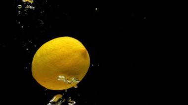 Sarı limon ve yeşil kireç siyah zemin üzerinde saydam suya dökülüyor. Akvaryumda taze meyve ve böğürtlen sıçraması. Citrus, sağlıklı yiyecekler, diyet, hava kabarcıkları. Ağır çekim. Yakın plan..