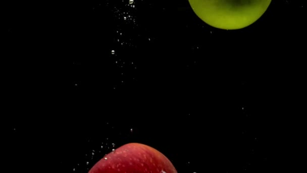 红色和绿色的苹果在黑色背景上落入透明水中 新鲜的水果和浆果在水族馆里飞溅 有机水果 健康食品 慢动作 — 图库视频影像