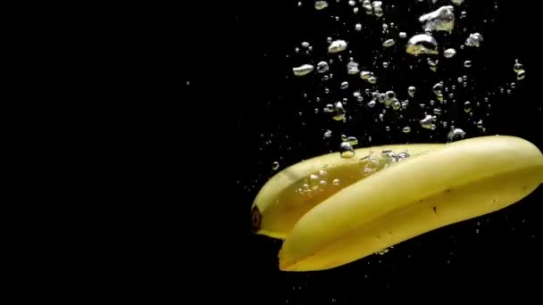 黒い背景に透明な水に落ちる2つの黄色いバナナ 水族館で飛び散る新鮮な果物やベリー オーガニックベリー 健康食品 ダイエット スローモーション クローズ アップ — ストック動画