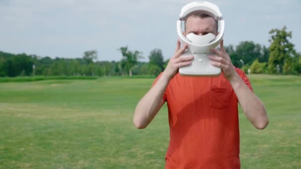 一个男人在公园里把Vr耳机戴在头上 一个穿着红色T恤和头盔的年轻人正在大自然的背景中体验虚拟现实 框架右侧的人 — 图库视频影像