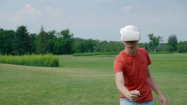 Bir adam VR kulaklık kullanarak ve parkta sanal bir oyun oynuyor. Kask genç adam doğanın arka planda artırılmış gerçeklik yaşıyor. Doğru çerçevede bir insan. 4k görüntüleri.