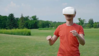 Bir VR kulaklık kullanan bir adam ve parkta sanal bir oyunda bir araba sürücü. Kask genç adam doğanın arka planda artırılmış gerçeklik yaşıyor. Doğru çerçevede bir insan. 4k görüntüleri.