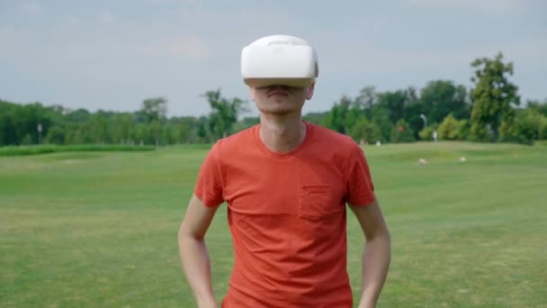 男は彼の頭の上にVrヘッドセットを置き 公園で仮想ゲームをプレイ 自然を背景に拡張現実を体験ヘルメットの若い男 フレームの中央に人間 4Kフッテージ — ストック動画