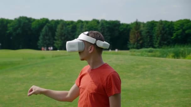 Vrヘッドセットを使用し 公園で仮想ゲームをプレイする男 自然を背景に拡張現実を体験ヘルメットの若い男 ダイナミック撮影 4Kフッテージ — ストック動画