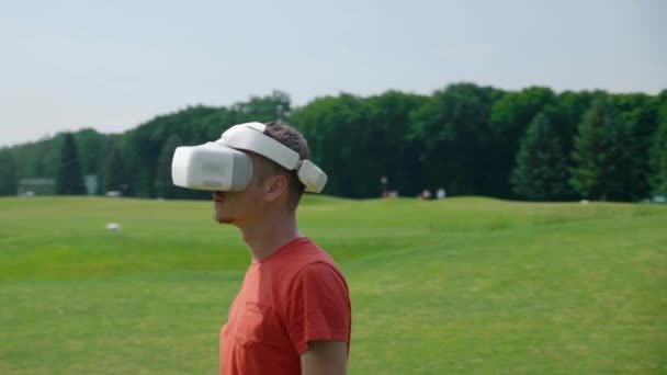 Vrヘッドセットを使用している男は 周りを見回し 公園で仮想ゲームをプレイしています 自然を背景に拡張現実を体験ヘルメットの若い男 ダイナミック撮影 4Kフッテージ — ストック動画