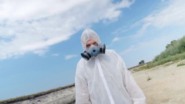 身着防护服 戴着防毒面具的男子正站在被塑料污染的河湖岸边 框架旋转 生态灾难 人为影响 拯救地球4K — 图库视频影像