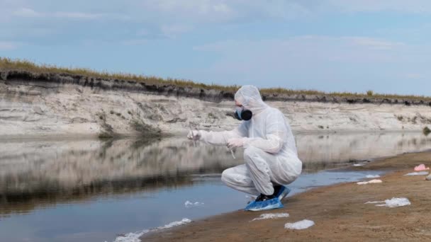 복장과 호흡보호구의 방독면을 남자가 시험관에서 샘플을 검사한 호수에 붓습니다 과학자는 — 비디오