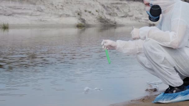 身着防护服和呼吸器防毒面具的男子观察试管中水的化学反应 他从一条被污染的河流湖中进行分析 科学家在体外取样 — 图库视频影像