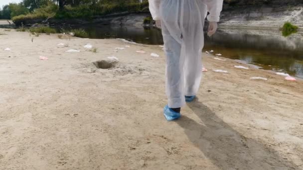穿着防护服的男子双腿的特写 他沿着一条干涸的河流行走 估计污染的程度 人类正在毒害地球 生态灾难 — 图库视频影像