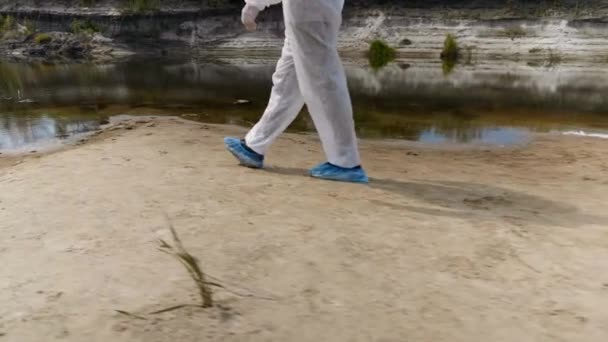 乾いた川に沿って歩き 汚染の程度を推定する防護服を着た男性の足のクローズアップ 人類は地球を汚染している生態学的な大きなトロフィー4K — ストック動画