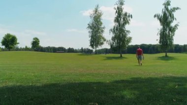 Elinde sanal gerçeklik kulaklığı olan bir adam ağaçların arasında yeşil çimenler boyunca yürür ve kameraya döner. 4k drone görüntüleri.