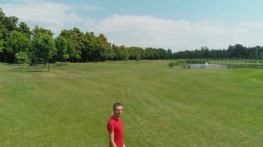 Elinde sanal gerçeklik kulaklığı olan, güzel ağaçlar ve ormanlar arasında yeşil çimenler boyunca yürüyen, yaz aylarında güneşli bir günde bulutlarla mavi gökyüzüne sahip bir adamın havadan görünümü. 4k drone görüntüleri.