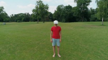 Kafasını kıp parktaki kameraya bakan Vr kulaklı adamın havadan görüntüsü. Kasklı genç adam doğanın arka planında artırılmış gerçeklik yaşıyor. 4k drone görüntüleri.