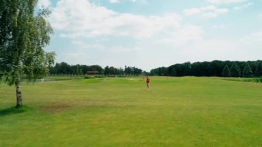 Elinde sanal gerçeklik kulaklığı olan, güzel ağaçlar ve ormanlar arasında yeşil çimenlerin üzerinde duran, yaz aylarında güneşli bir günde bulutlarla mavi gökyüzü nereli bir adamın havadan görünümü. 4k drone görüntüleri.