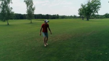 Vr kulaklık kullanan ve parkta sanal bir oyun oynayan bir adam. Kasklı genç adam doğanın arka planında artırılmış gerçeklik yaşıyor. Çerçevenin sağ tarafında bir insan var. 4k drone görüntüleri.