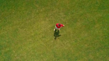 Elinde sanal gerçeklik kulaklığı olan, güzel ağaçlar ve ormanlar arasında yeşil çimenlerin üzerinde duran, yaz aylarında güneşli bir günde bulutlarla mavi gökyüzü nereli bir adamın havadan görünümü. 4k drone görüntüleri.