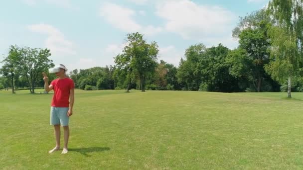 彼の頭の上にバーチャルリアリティヘッドセットを持つ男は立って 夏の時間に晴れた日に雲と緑の草の上にVrヘルメットを使用しています 4Kドローン映像 — ストック動画