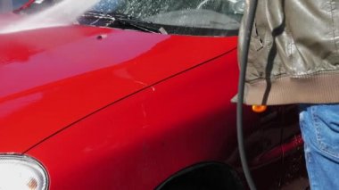 Self servis araba yıkamada araba yıkayan adam. Yüksek basınçlı bir su jeti otomobildeki kiri temizler. Köpüklü deterjan arabanın kaputundan boşaltılır. 4k görüntü.