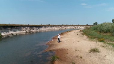 Koruyucu giysili bir adamın havadan görünümü ve kuru ve kirli bir nehrin kıyısında arka planda bir kuş la plastik çöp toplayan bir solunum cihazı. Ekolojik felaket. 4k drone görüntüleri.