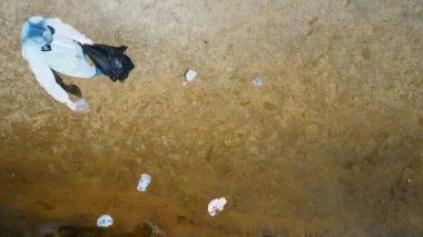 Koruyucu giysili bir adamın havadan görünümü ve kuru ve kirli bir nehrin kıyısında plastik çöp toplayan bir solunum cihazı. Ekolojik felaket. Antropojenik etki. 4k drone görüntüleri.