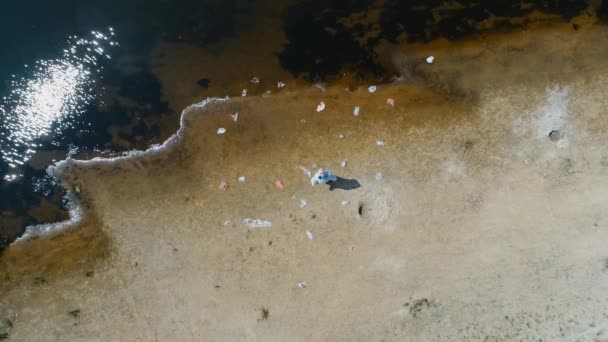 防護服を着た男と 乾燥した汚染された川のほとりにプラスチック廃棄物の間に立ち 見上げる人工呼吸器の空中写真 生態学的な大きなトロフィー4Kドローン映像 — ストック動画