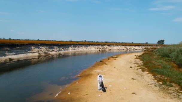 保護スーツを着た男と 乾燥した汚染された川のほとりにプラスチックゴミを集める人工呼吸器の空中写真 生態学的な大きなトロフィー人為的影響4Kドローン映像 — ストック動画
