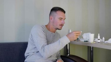 Hasta adam evde kendi kendine ilaç kullanıyor. Üzgün genç adam kanepede oturuyor ve hapların adını okuyun. Başucunda bir sürü ilaç var. Akut Solunum Yolu Virüsü Enfeksiyonu. Hastalık soğuk algınlığı. 4k