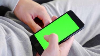 Adam evde kanepede oturan ve yeşil maket ekran ile akıllı telefon kullanarak. Adam kanepeye uzanmış, cep telefonuyla swiping yapıyor. Kaydırma hareketleri. Internet Sosyal Ağlar Tarama. Close. 4k