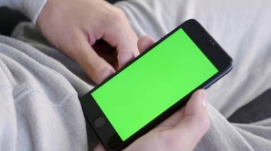 Adam evde kanepede oturan ve yeşil mock-up ekran akıllı telefon tutarak. Adam kanepede yatıyor, cep telefonu alıyor. Internet Sosyal Ağlar Tarama. Modern telefon. Close. 4k görüntü.
