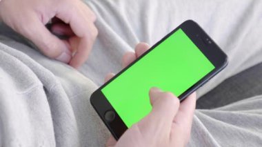 Adam evde kanepede oturan ve yeşil maket ekran ile akıllı telefon kullanarak. Adam kanepeye uzanmış, cep telefonuyla swiping yapıyor. Kaydırma hareketleri. Internet Sosyal Ağlar Tarama. Close. 4k