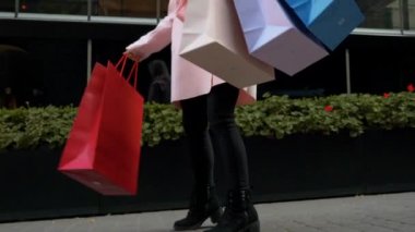 Genç çekici kadın alışveriş. Elinde kağıt torbalar olan bir bayan, Alışveriş Merkezi'nin cephesinin yeşil çiçek tarhının arka planına karşı sokakta dans ediyor. Noel tatili, satış, perakende sektörü konsepti.