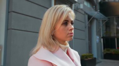 Alışveriş Merkezi'nin arka planına karşı sokakta duran pembe ceketli genç çekici sarışın kadının portre fotoğrafı. Noel tatilleri, alışveriş, satış ve perakende sektörü konsepti. 4k görüntü.